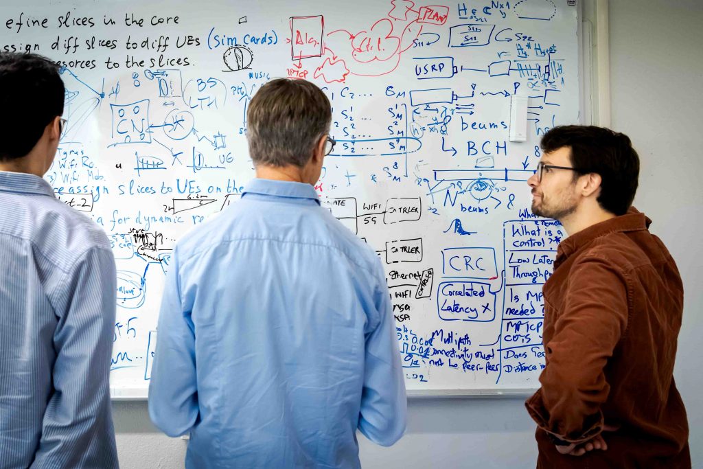 Three men looking at whiteboard calculations.
